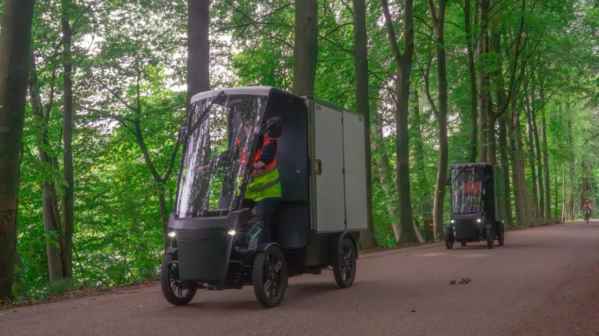 Two micromobility carts drive along a forested path. 