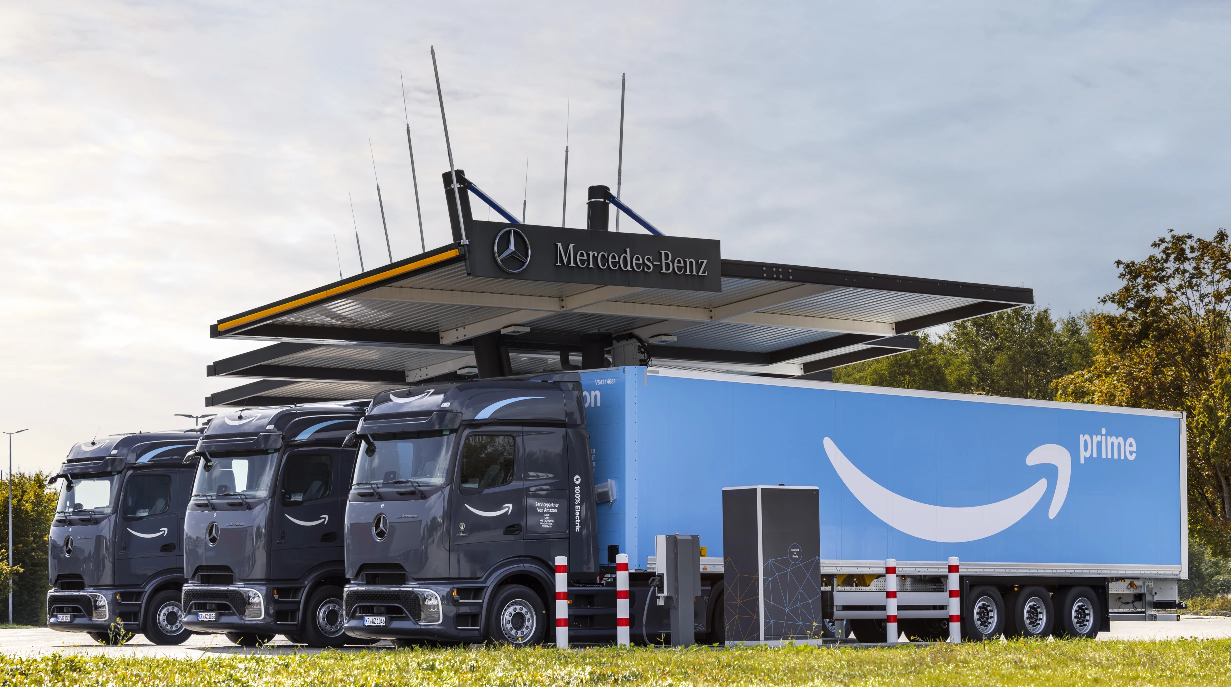 Three electric semitrucks parked under a Mercedes-Benz sign. 