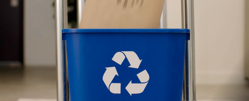 A recyclable paper padded mailer gets put into a blue recycling bin.