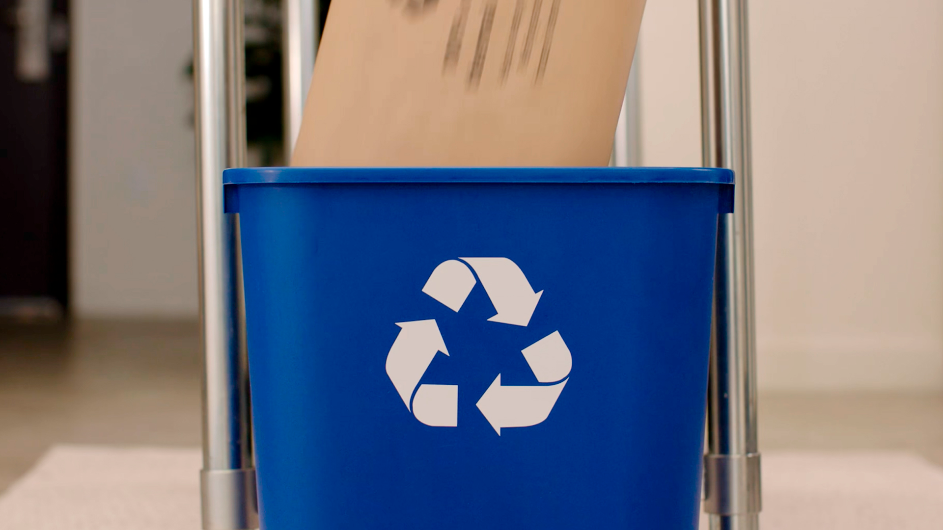A brown package is placed in a blue recyling bin. 