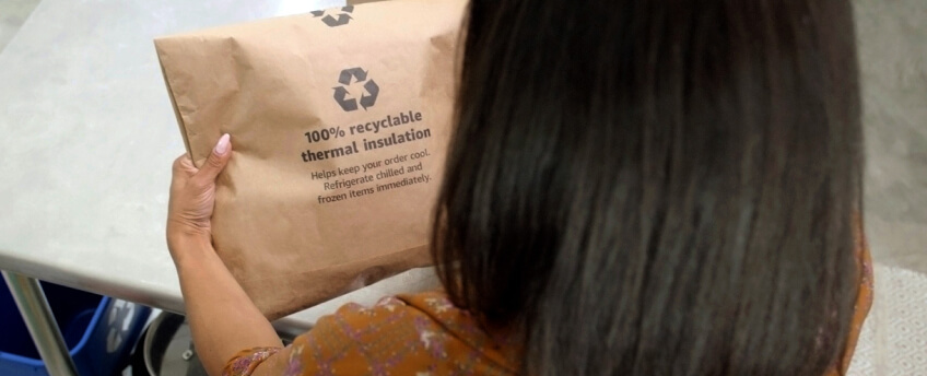 A person pulls an item out of a recylable paper padded mailer, and puts the empty mailer into the recycling bin. 