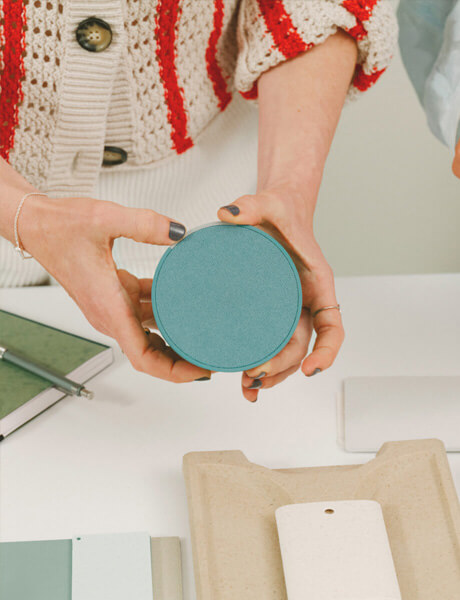 A person holds a blue circular device over a table with design materials. 