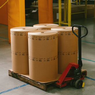 Four large rolls of paper material sit on a pallet jack.