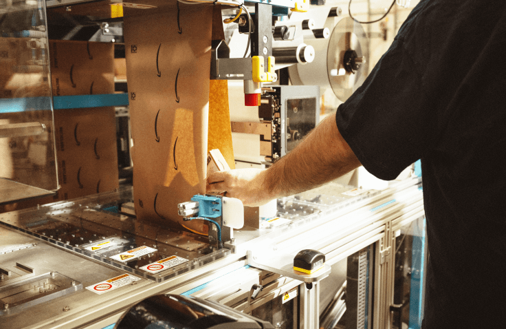 A person uses a machine to assemble packaging around a product. 