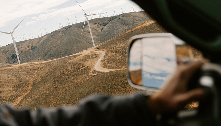 A view from the inside of a vehicle shows wind turbines along a dry hillside beneath text about "First mile" transportation. 