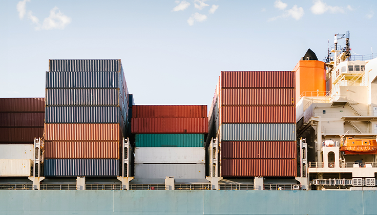 Shipping containers are shown neatly stacked on a ship deck beneath text about "First mile" transportation. 