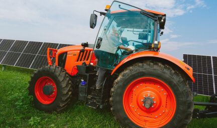 A tractor drives through a grassy path between solar panels