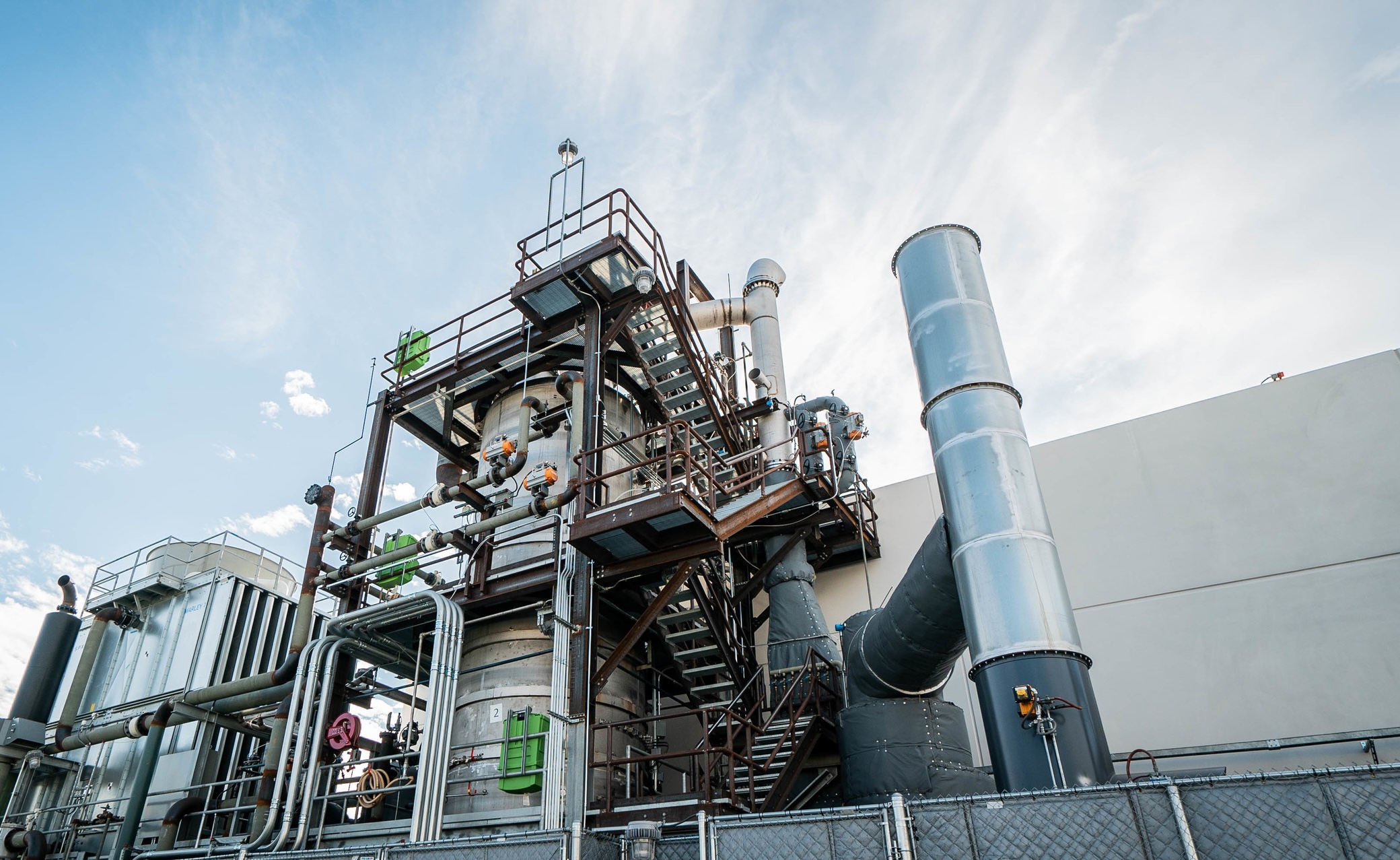 A view of the outside of a building, with many pipes and a staircase. 