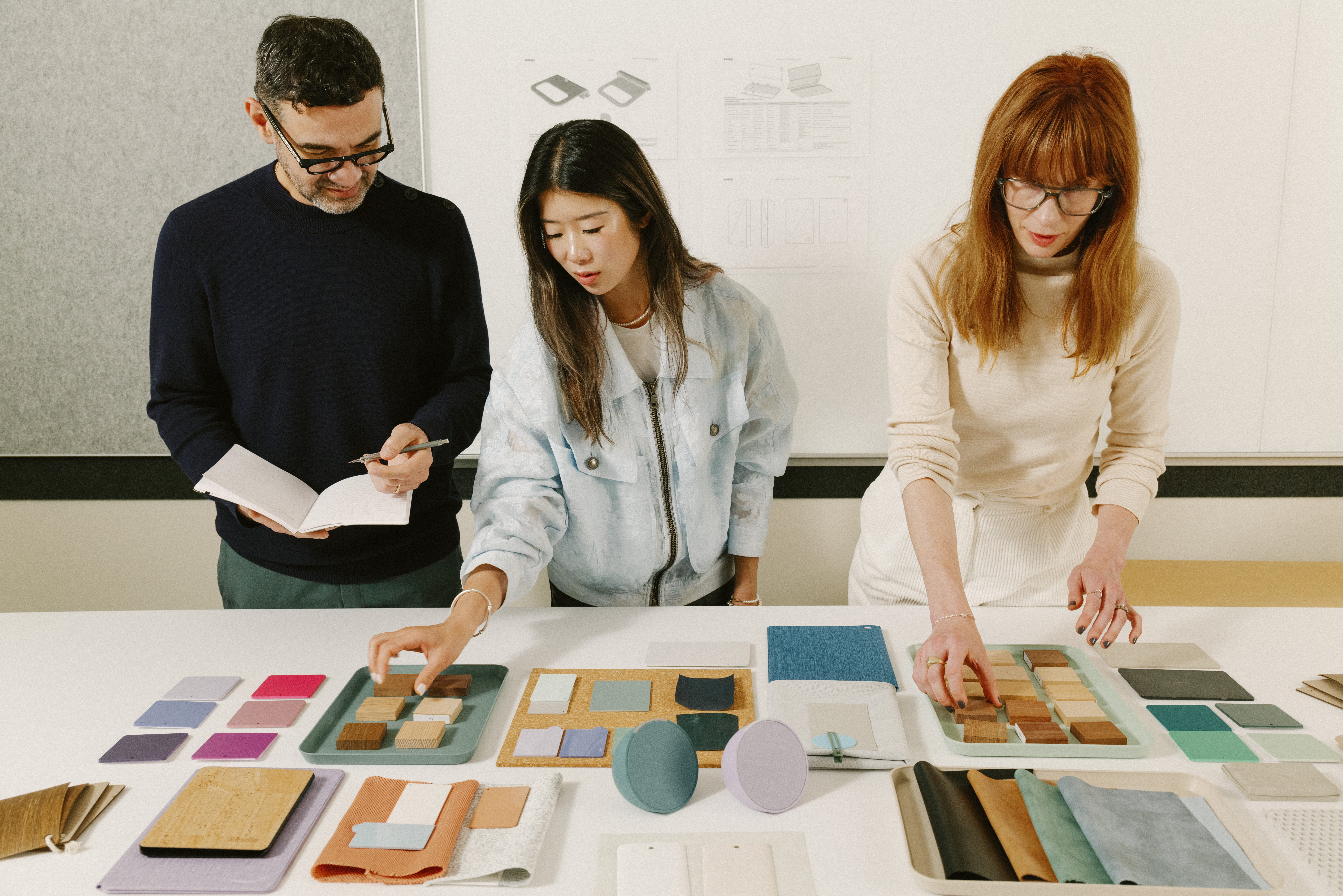 Three people stand at a table, looking through organized fabric samples.