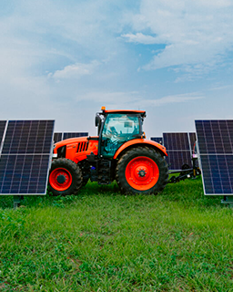 A tractor drives in front of rows of solar panels in a green field.