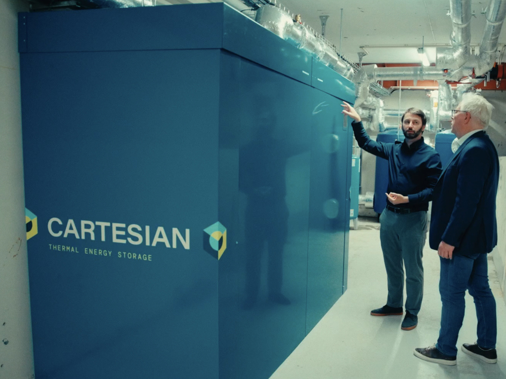 Two people stand next to thermal energy storage unit. 
