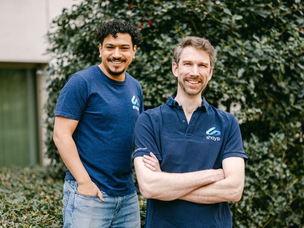 Two people in blue shirts stand smiling for a photo. 