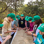 A group of children wearing green hats gather around and inspect a piece of cloth.