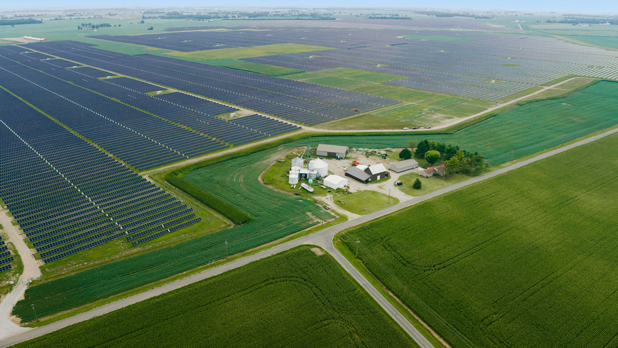 An overhead view of farmland surrounded by rows of solar panels.