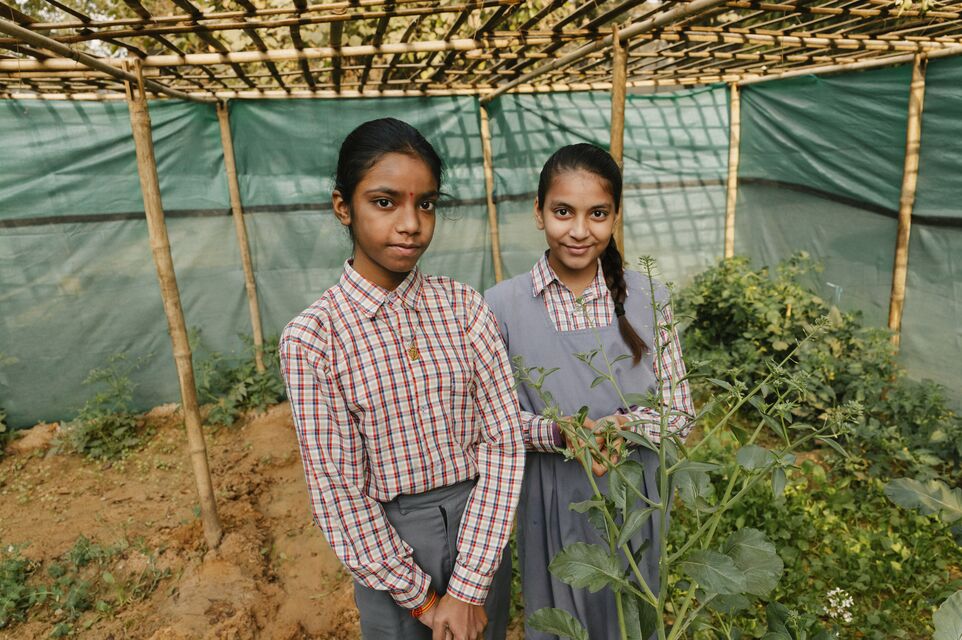 Two girls stand smiling, looking at the camera.