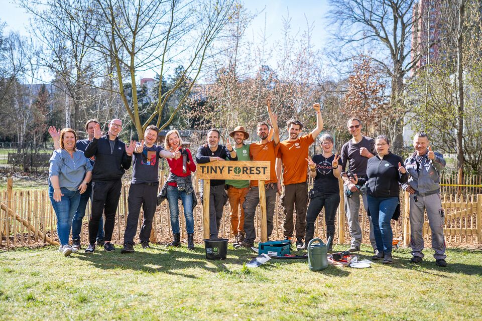 A group of people stand behind a sign that says: "tiny forests"