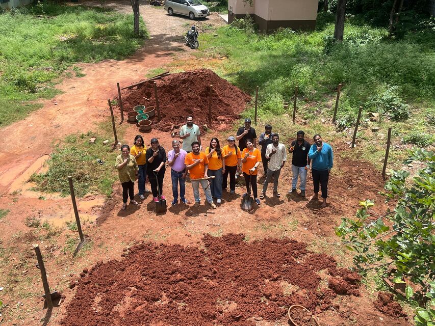 A group of people stand in a field smiling at an aerial camera.