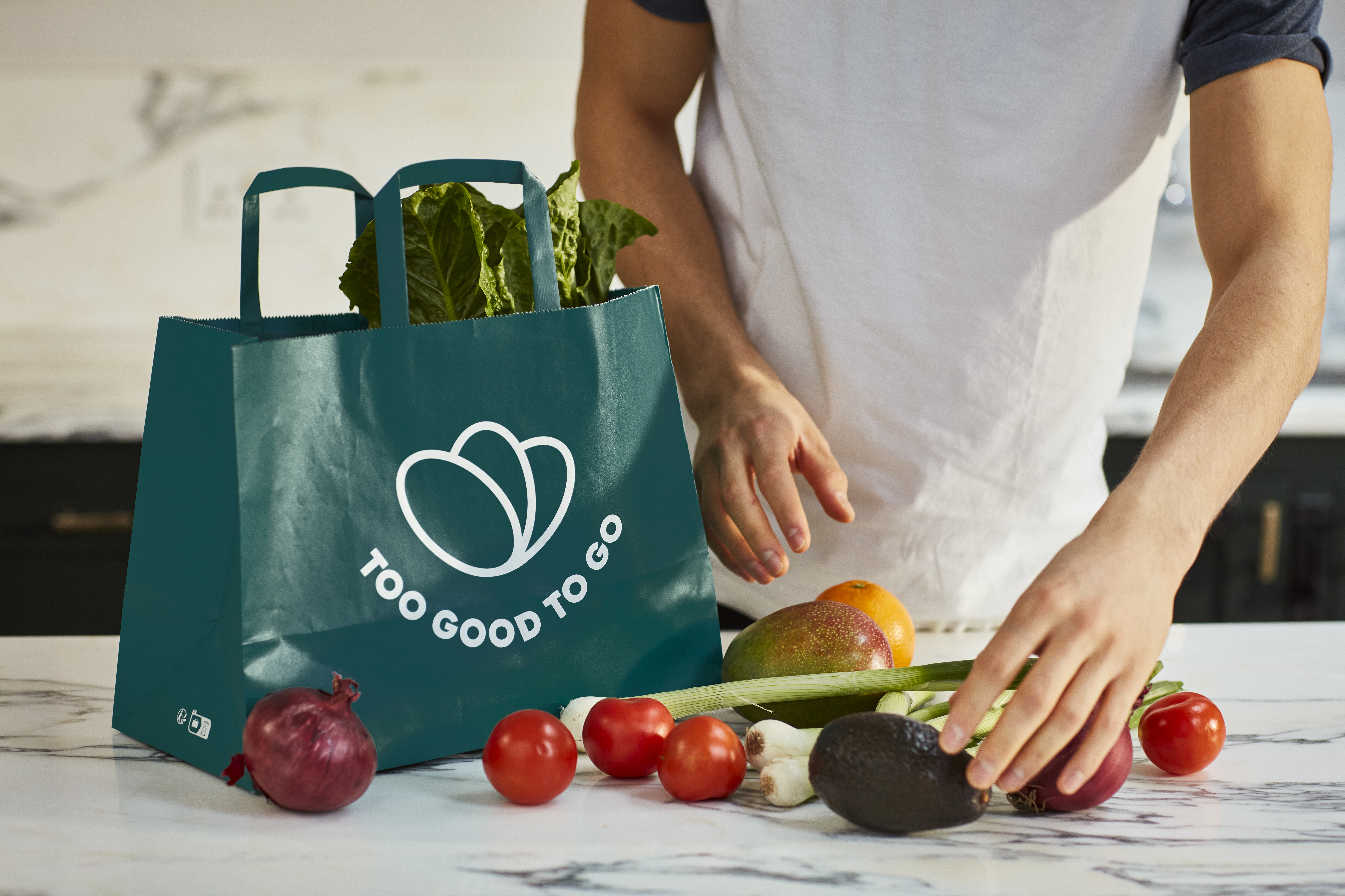 A person takes produce, including tomatoes, onions, and avocados out of a reusable tote bag.