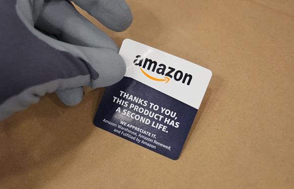 A gloved hand holds a sticker with the Amazon logo and text that says "Thanks to you, this product has a second life."