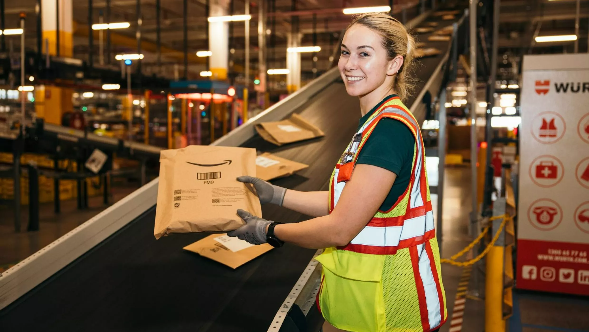 A person wearing a yellow safety vest stands smiling holding a paper mailer.