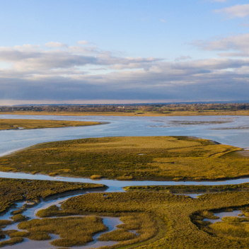 Partly cloudy skies over water ways running through garsslands. 