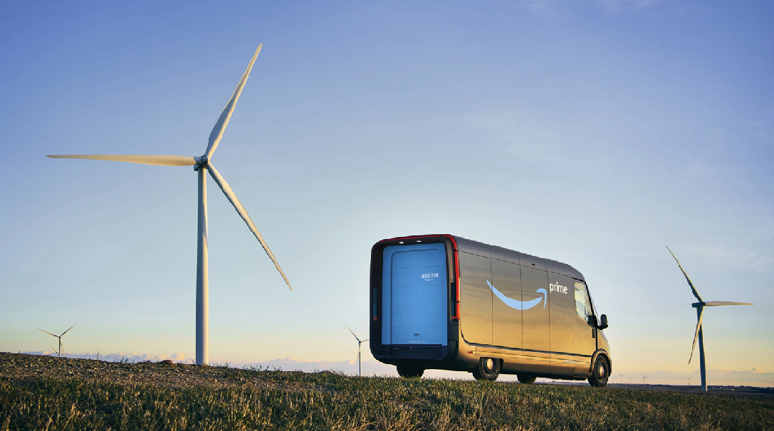 A delivery vehicle drives down a road at sunset alongside wind turbines. 