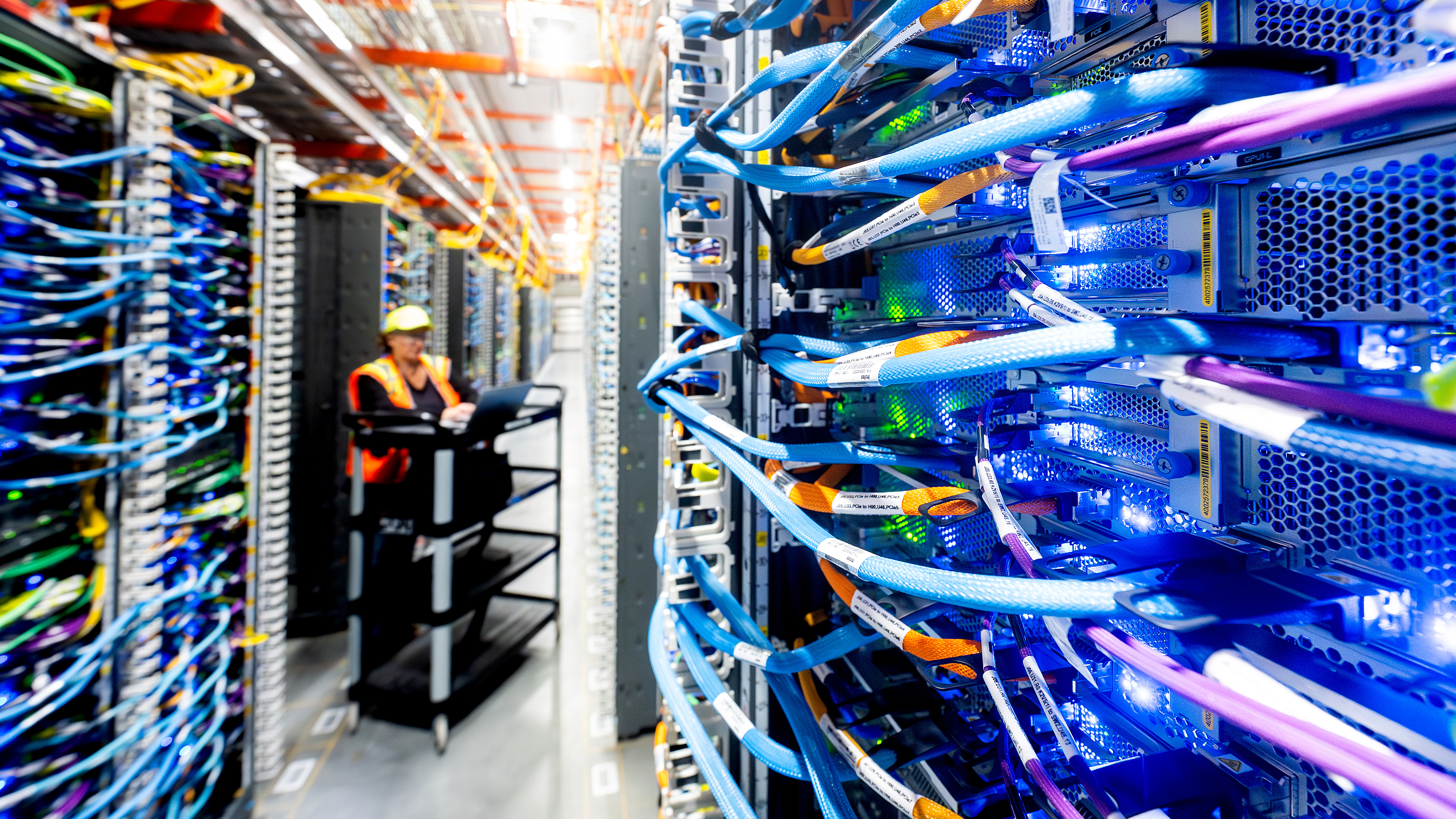 A person wearing safety equipment stands between racks of equipment. 