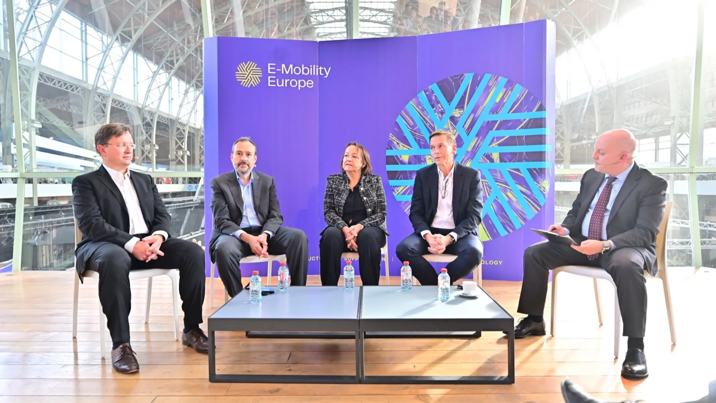 People sit in a panel in front of a wall that says "E-Mobility Europe."