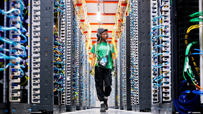 A person wearing safety gear walks between racks of equipment. 