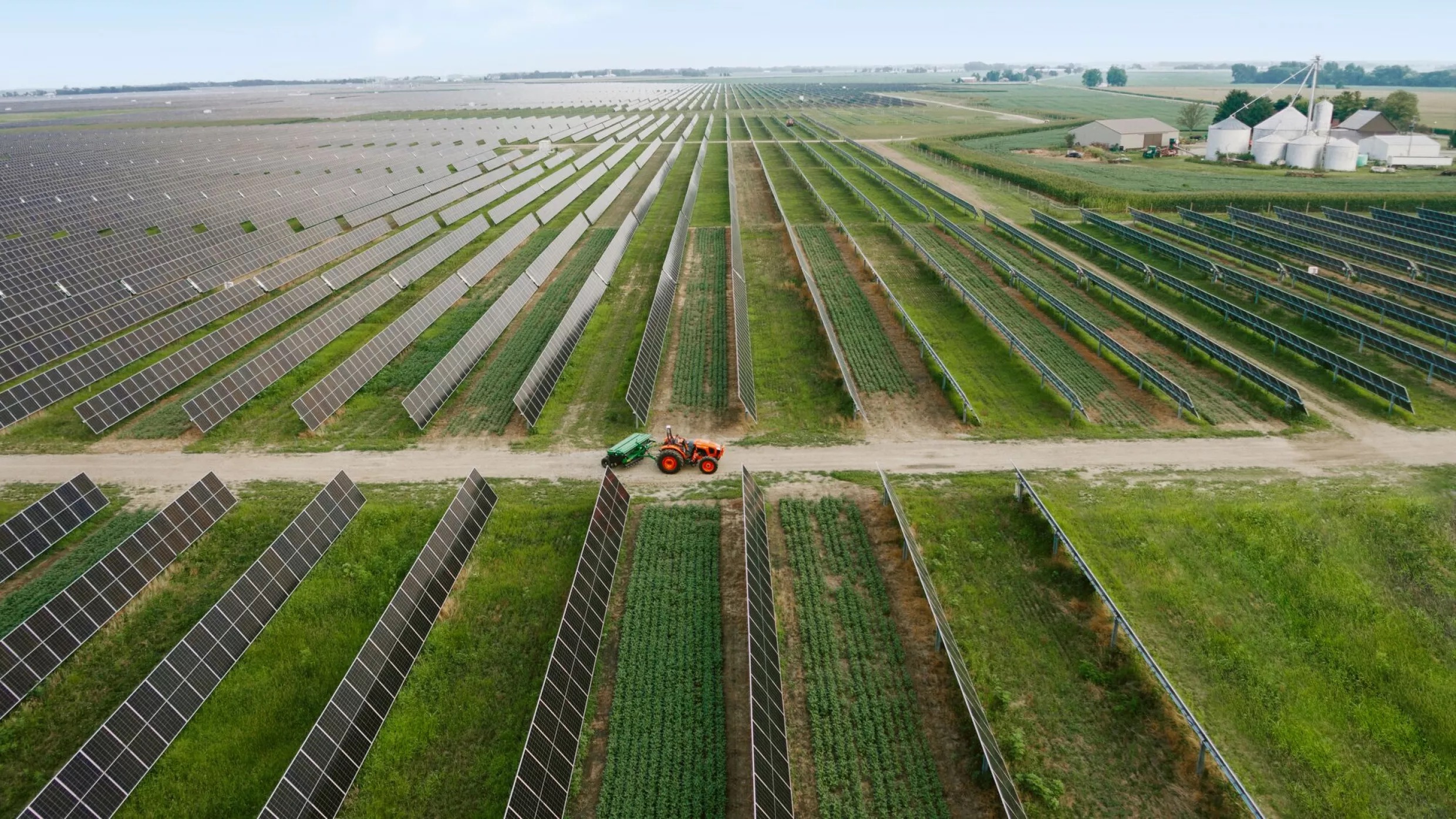 An aerial view of a tractor driving between rows of solar panels. 