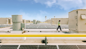 A person walks on the roof of a building with solar panels. 