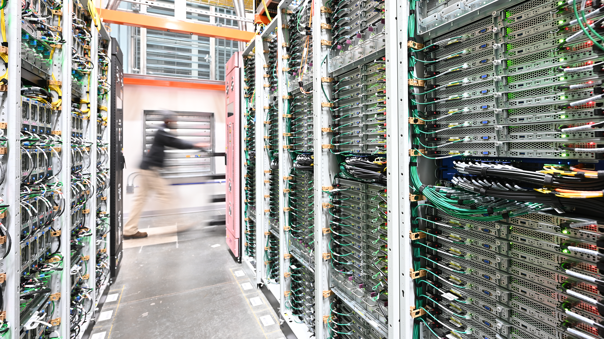 A person pushing a cart walks past racks of equipment.