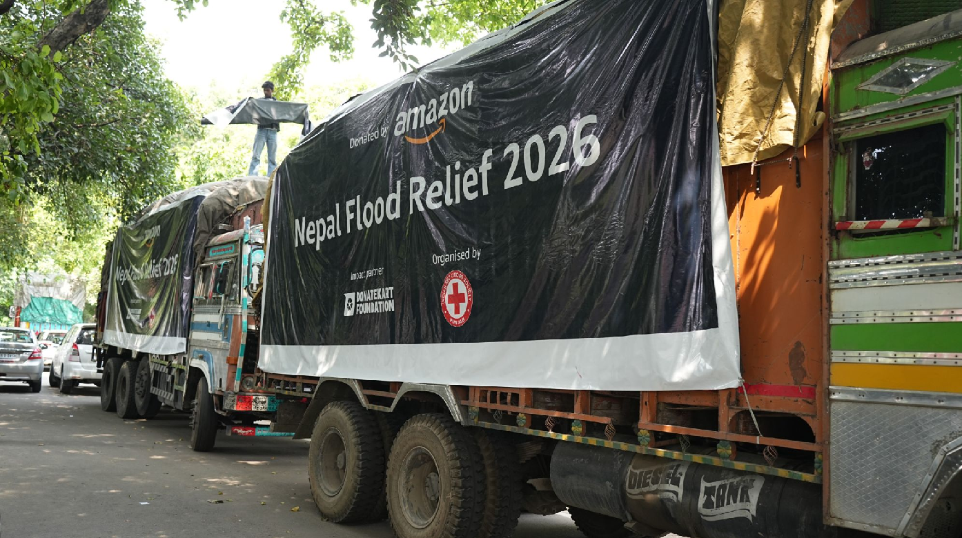 Two trucks drive down a street covered by banners that say: "Nepal Flood Relief 2026." 