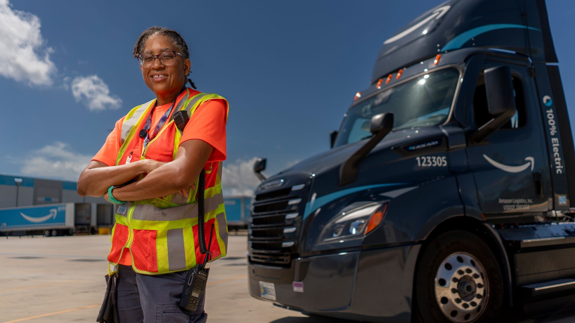 A person in an orange vest stands in front of an Amazon truck. 