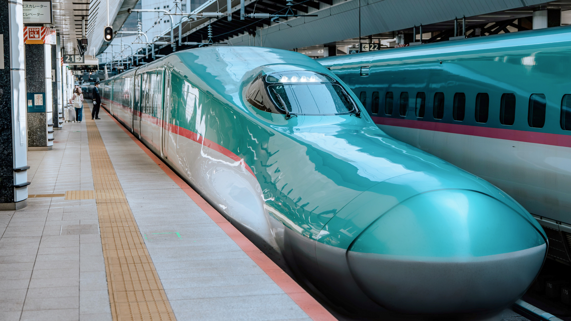 A bullet train pulls into a station next to a long platform. 
