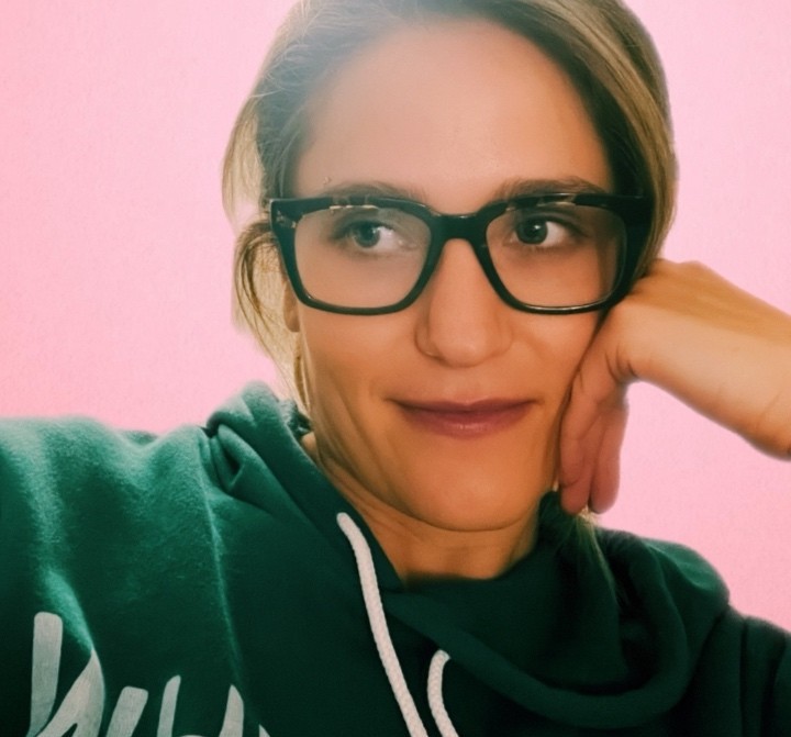 A woman smiling in front of a pink background.