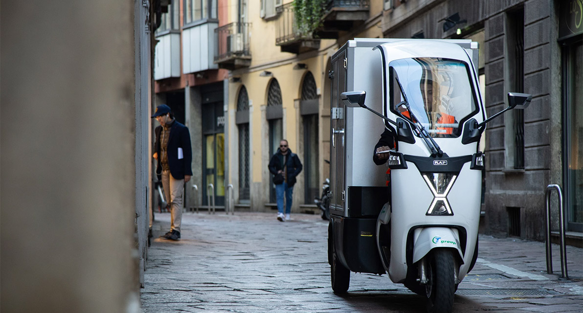 A person drives an electric moped down  a narrow cobblestone street. 