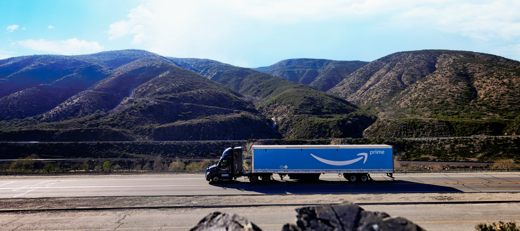 A truck driving on a road in front of hills. 