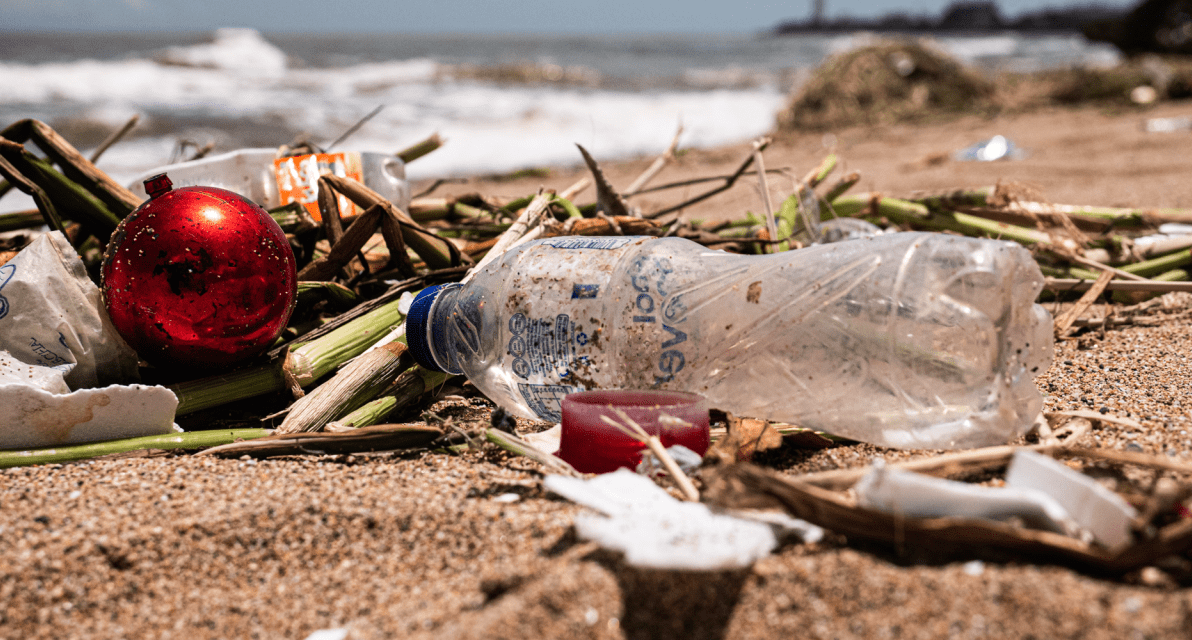 A plastic water bottle is shown amongst other trash items on a beach. 