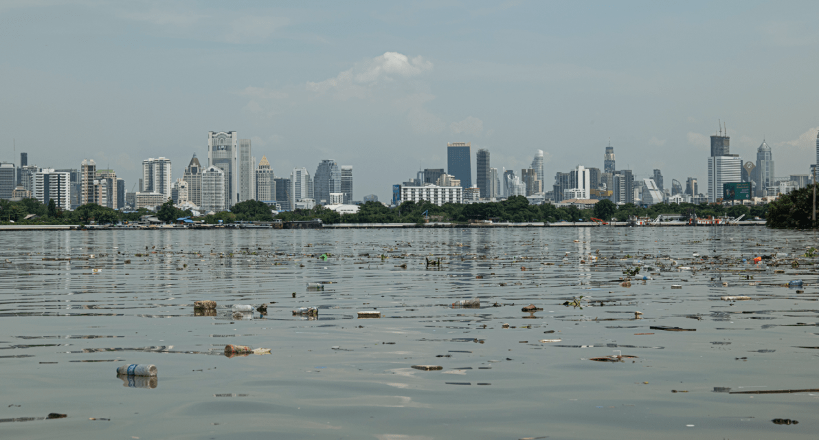 A city skyline is shown in the distance behind trash scattered on the surface of surrounding waters. 