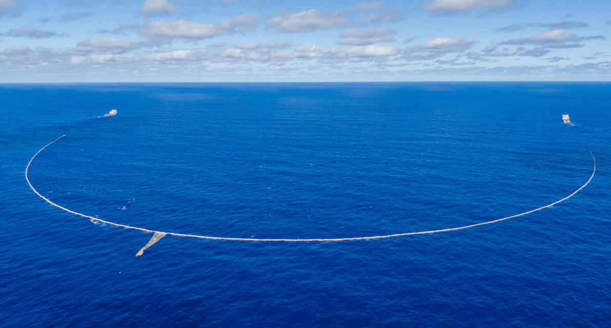 An aerial view shows the end-to-end size of a large net collecting trash in the ocean. 