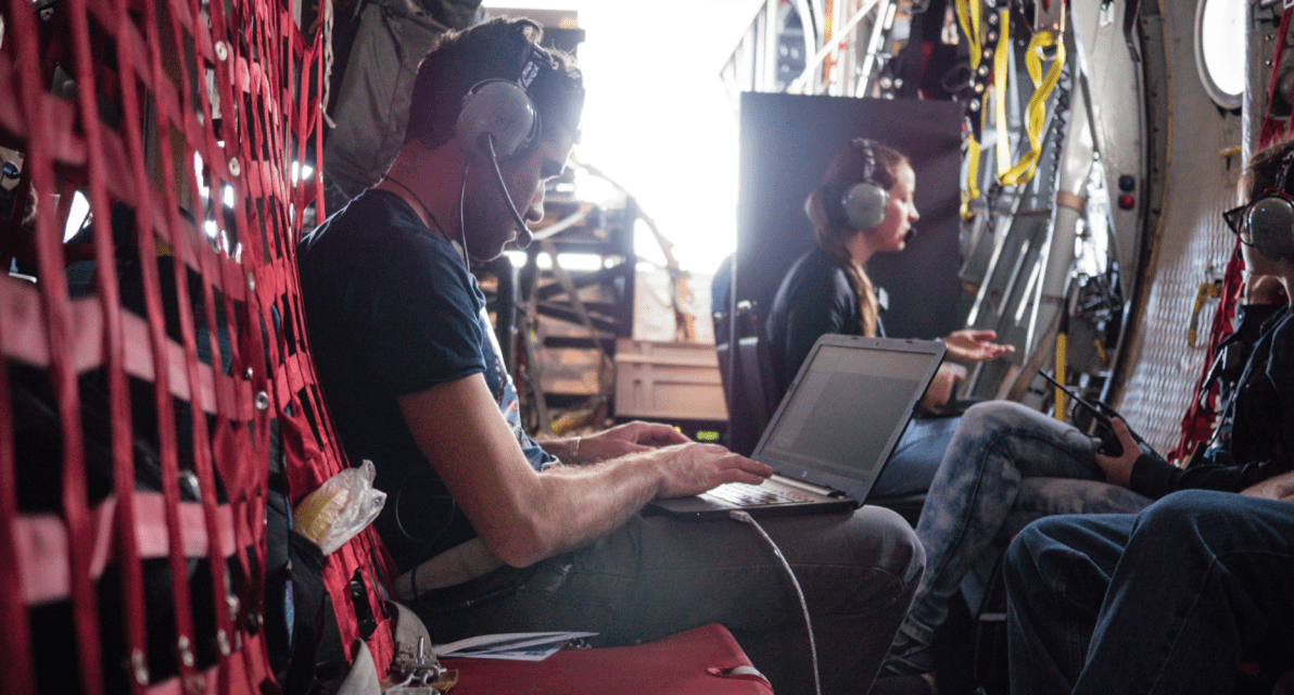 A person sitting next to a red net uses a laptop. 