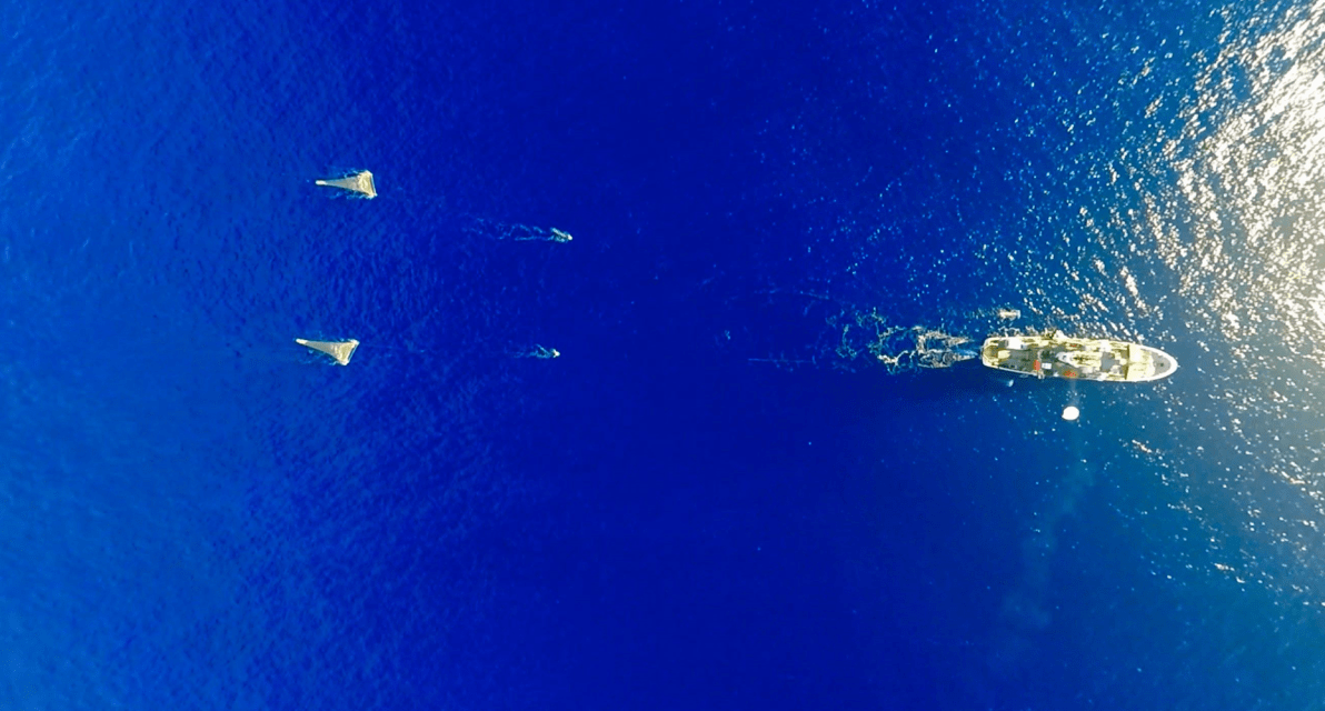 An aerial view of a boat pulling nets behind it in the ocean. 