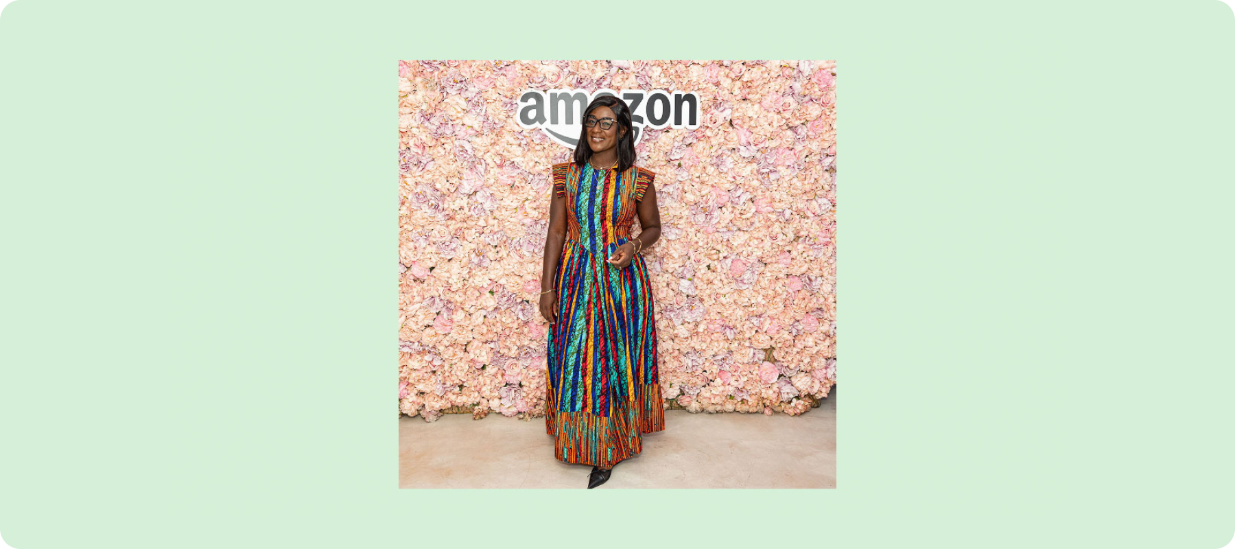A person stands smiling in front of a pink background with text that says "Amazon." 
