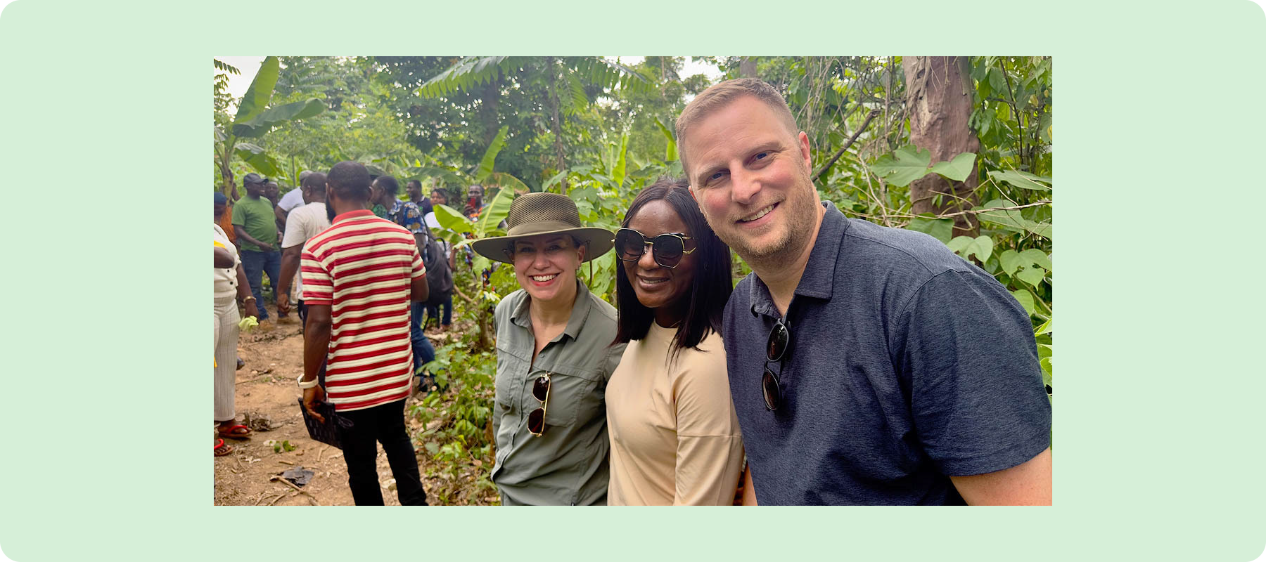 Three people smiling, huddled together in a forest setting. 