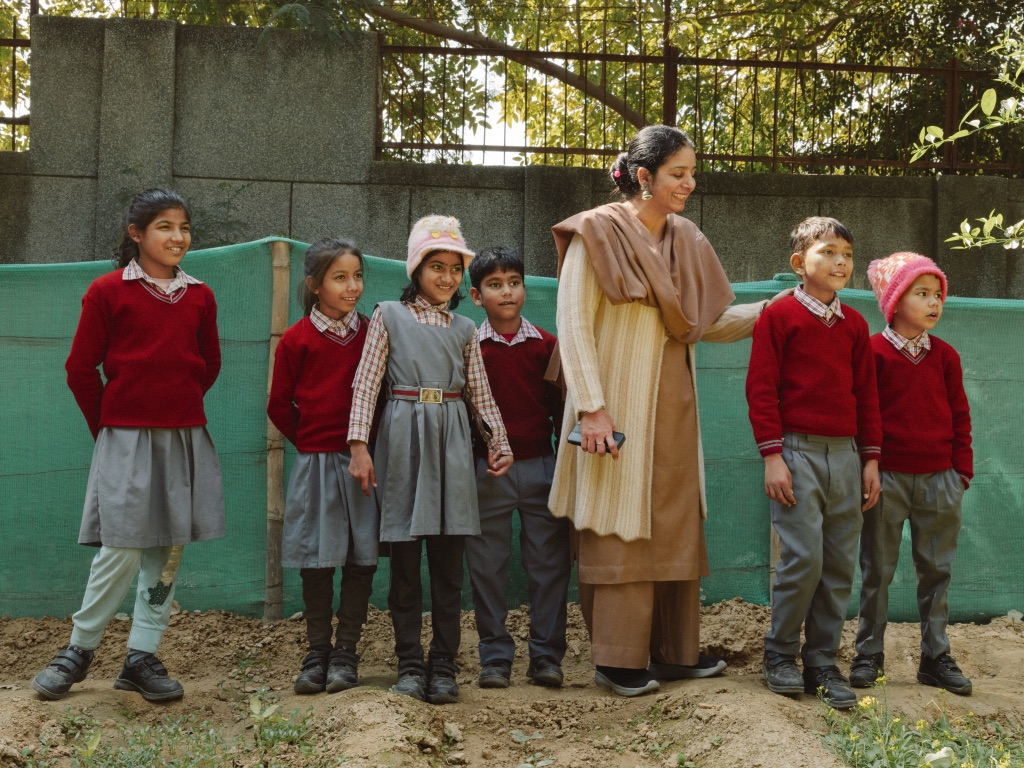 Students in red school uniforms stand with their teacher in an outdoor garden space.