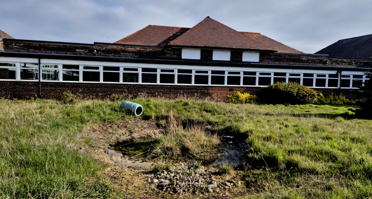A brick building sits on a grassy hillside. 