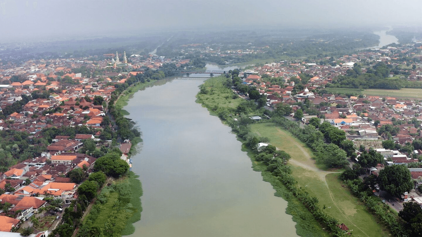 A river winds through a town with red-roofed buildings. 