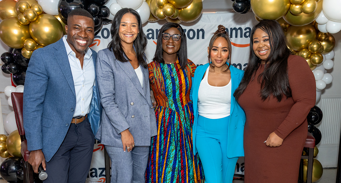 A few speakers are seated on a stage, with an audience listening sitting around round tables. 