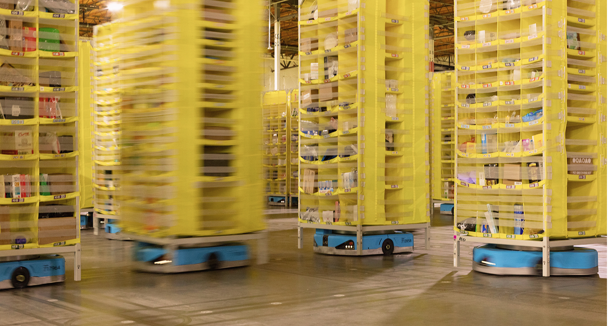 Yellow shleving towers full of items are moved across a warehouse floor using robotic devices. 